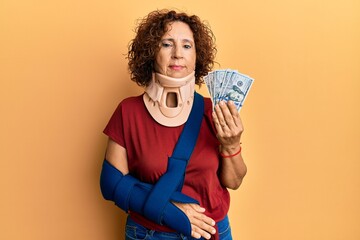 Beautiful middle age mature woman wearing cervical collar and sling holding insurance dollars...