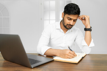 Close up photo of smart successful indian businessman ceo worker work on laptop make notes in copybook