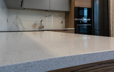 White kitchen countertop, marble backsplash, gray kitchen cabinets, black kitchen appliances. Metal tap and liquid soap dispenser.