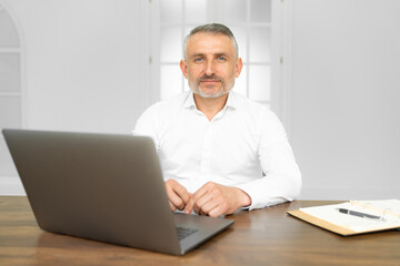 Middle age handsome businessman wearing tie sitting using laptop at the office with serious expression on face