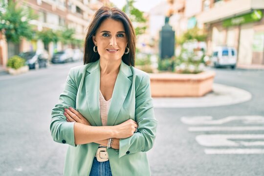 Confident business woman wearing elegant suit standing at the street with cheerful face and arms crossed