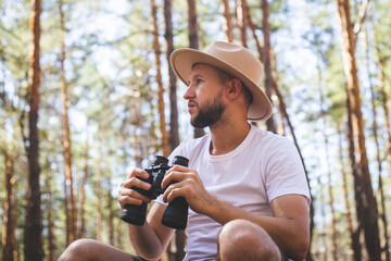 Man in a hat holds binoculars during a camping trip. Hike in the mountains, forest