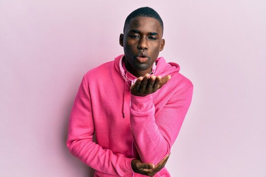 Young african american man wearing gym clothes and using headphones looking at the camera blowing a kiss with hand on air being lovely and sexy. love expression.