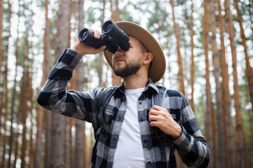 Male tourist looking through binoculars in the forest