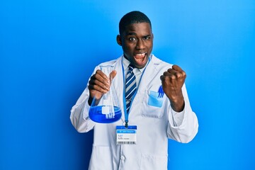 Young african american man wearing scientist uniform holding test tube screaming proud, celebrating victory and success very excited with raised arms