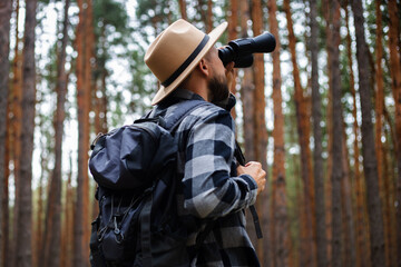 Fototapeta premium Male tourist looking through binoculars in the forest