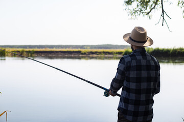 Man in a hat and a plaid shirt is fishing on a line by the river