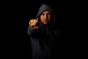 Man in a hood points a finger against a dark background
