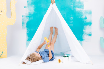 Portrait of a beautiful smiling girl with a paint roller. Little girl playing in a white wigwam on a background of colorful walls. Cheerful cute baby having fun in the nursery. baby's day. © Andriy Medvediuk