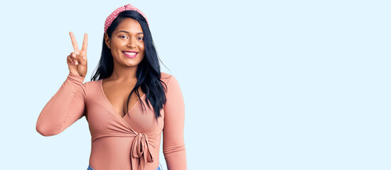 Hispanic woman with long hair wearing casual clothes smiling with happy face winking at the camera doing victory sign. number two.