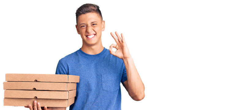 Young handsome hispanic man holding delivery pizza box doing ok sign with fingers, smiling friendly gesturing excellent symbol