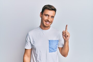 Handsome caucasian man wearing casual clothes smiling with an idea or question pointing finger up with happy face, number one