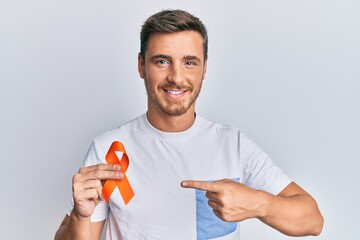 Handsome caucasian man holding awareness orange ribbon smiling happy pointing with hand and finger