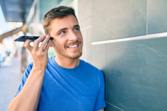 Young caucasian man smiling happy listening audio message using smartphone at the city.