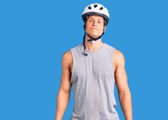 Young handsome man wearing bike helmet relaxed with serious expression on face. simple and natural looking at the camera.