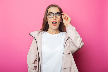 Surprised young woman in pink jacket, pink isolated background