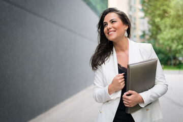 Beautiful business woman holding folder in front of corporate building. Smiling confident female manager