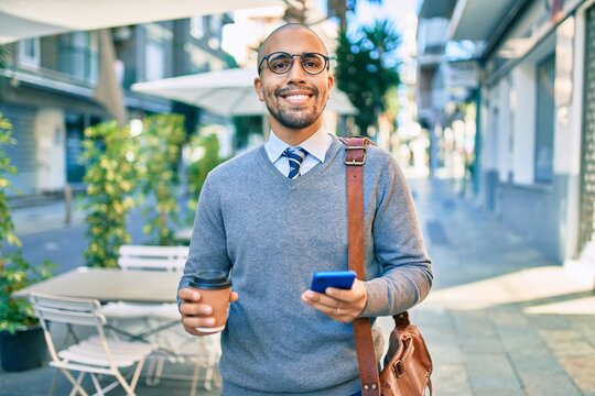 Young african american businessman using smartphone and drinking take away coffee at the city.
