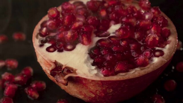 Half a ripe red pomegranate on a dark background close-up, approaching the camera . High quality FullHD footage