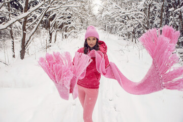woman in pink clothes a jacket a knitted scarf and a hat stands in a snowy forest in winter