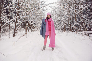 Fototapeta na wymiar woman in pink clothes a jacket a knitted scarf and a hat stands in a snowy forest in winter