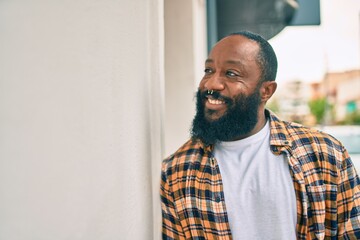 Handsome modern african american man with beard smiling positive leaning over wall