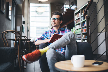 Fototapeta premium Positive young man reading daily planner and drinking coffee in coffee shop
