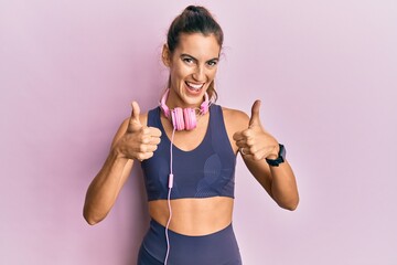 Young beautiful woman wearing gym clothes and using headphones success sign doing positive gesture with hand, thumbs up smiling and happy. cheerful expression and winner gesture.