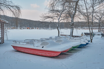 A view of the snow-covered colored pedal boats, the frozen lake and the city beach.