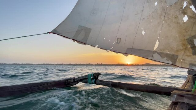 Old traditional maritime traditional vessel Dhow boat sailing under torned sail in the open Indian ocean near Zanzibar island in beautiful sunset time, Tanzania. Traveling 4K footage concept.