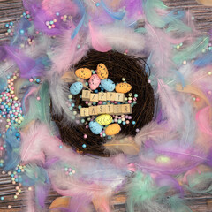 Colorful Easter eggs in bird nest surrounded with pastel colored feathers and wooden cubes with the text Happy Easter top view, modern background design, Easter holliday, Spring, concept