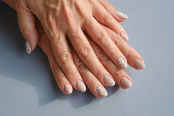 Hands of an adult woman with a new manicure. Hands with beige nail polish on a gray background. Shallow depth of field