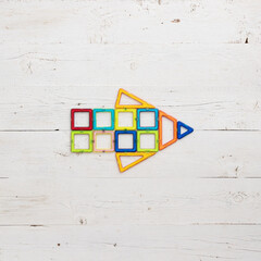 Arrow made of magnetic plastic parts of the constructor on a white wooden background