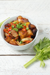 Diced cooked vegetables on light wood background in white plate. Healthy lunch - stewed garden vegetables. Traditional ratatouille with greens, zucchini, bell peppers and eggplant. Space for text