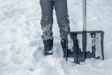 A snow shovel stands next to your booted feet.