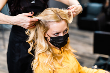 Fototapeta premium Beautiful hairstyle of middle-aged woman with protective face mask after dyeing hair in hair salon.