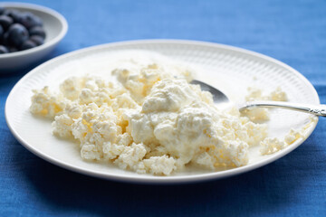 Plate of fresh cottage cheese, breakfast with dairy products, protein food. Blue Linen Crumpled Tablecloth, bright contrast, close up