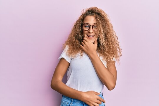 Beautiful caucasian teenager girl wearing white t-shirt over pink background looking confident at the camera smiling with crossed arms and hand raised on chin. thinking positive.