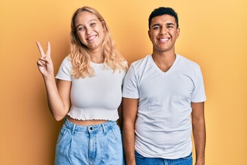 Young interracial couple wearing casual white tshirt showing and pointing up with fingers number two while smiling confident and happy.