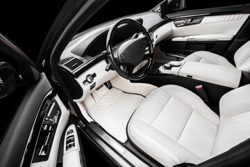 The car is inside. The interior of a prestigious modern car. Front seats with steering wheel, dashboard and display. white leather interior with black dashboard. on an isolated black background