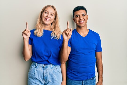 Young interracial couple wearing casual clothes pointing finger up with successful idea. exited and happy. number one.