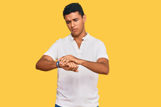 Young arab man wearing casual clothes checking the time on wrist watch, relaxed and confident