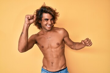 Fototapeta premium Young hispanic man standing shirtless dancing happy and cheerful, smiling moving casual and confident listening to music