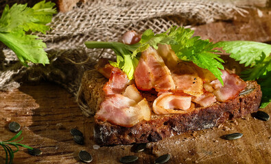 Sandwich with bacon and celery leaves on a slice of rye bread made from leaven with pumpkin seeds. Healthy food concept, traditional craft bread, close-up