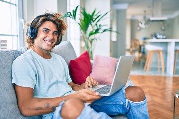 Young hispanic man smiling happy using laptop and headphones at home