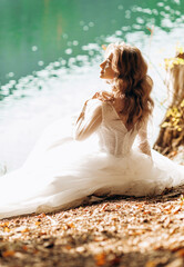 Fototapeta na wymiar Amazing bride sitting near the lake in the sun, caressing her face.