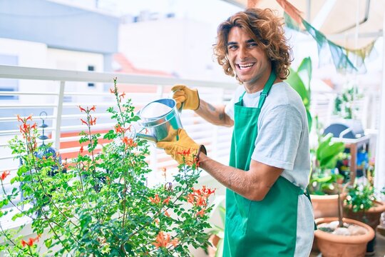 Young hispanic gardener smiling happy caring plants using watering can at terrace