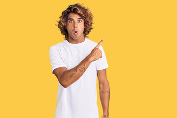 Young hispanic man wearing casual white tshirt surprised pointing with finger to the side, open...