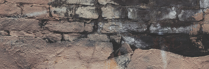 Old brick wall with peeling stucco. Weathered rough wall surface with brickwork. The wall is painted in different colors. Wide panoramic texture for background and design.