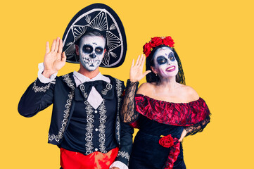 Young couple wearing mexican day of the dead costume over background waiving saying hello happy and smiling, friendly welcome gesture